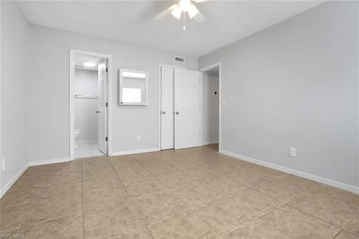 Unfurnished bedroom featuring visible vents, ensuite bathroom, light tile patterned floors, baseboards, and ceiling fan