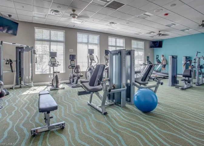 Fitness center featuring multiple exercise machines, patterned carpet, large windows, ceiling fans, and wall-mounted televisions