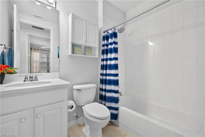 White vanity with white shaker-style cabinetry, and tiled tub/shower surround and tile flooring.