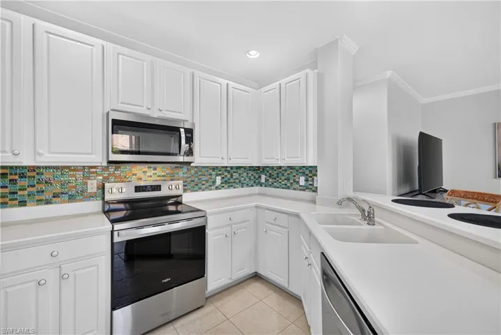 White cabinetry, stainless steel appliances, tile backsplash, white countertops, and recessed lighting.
