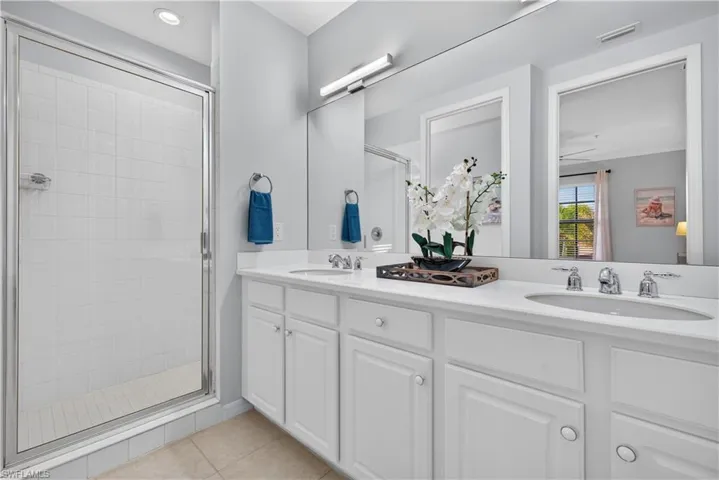 Dual vanity with white cabinetry, modern lighting, walk-in shower with tiled walls, tile flooring, a private water closet and a walk-in closet.