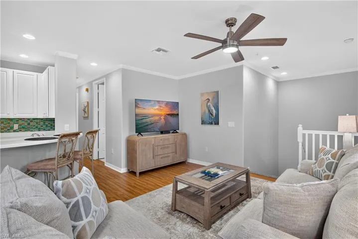 Crown molding, wood-finish laminate flooring, recessed lighting, and a ceiling fan with integrated light