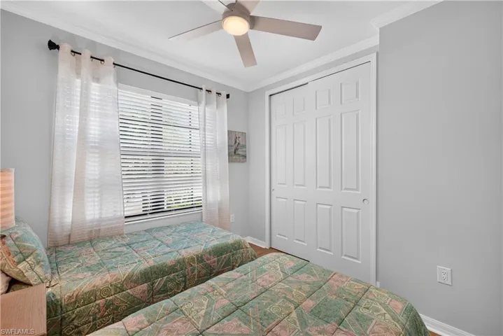 Guest bedroom with twin beds, curtains, blinds, ceiling fan with light and crown molding.