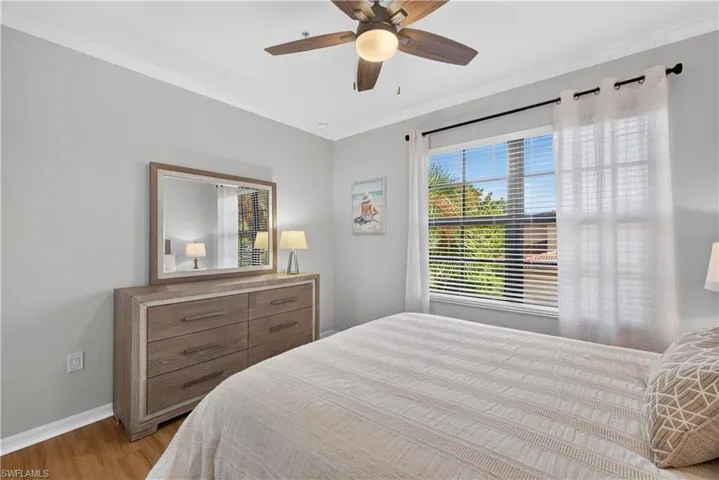 Wood-finish laminate flooring, crown molding, ceiling fan with integrated lighting, a large window with blinds and curtains.