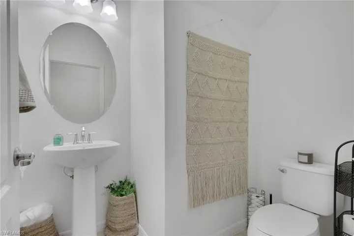 Oval wall-mounted mirror, pedestal sink with chrome faucet, and three-bulb vanity light fixture