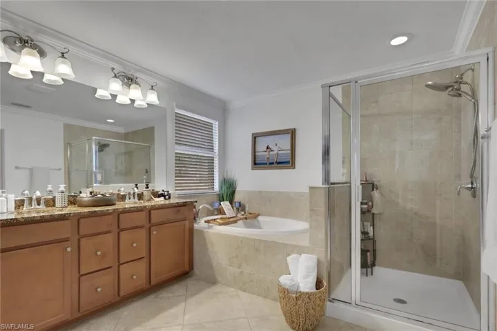 Bathroom featuring a double-sink vanity with stone countertop, drop-in soaking tub with stone surround, walk-in glass-enclosed shower, and large wall-mounted mirror