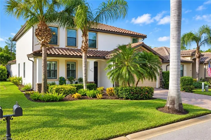 Stucco exterior featuring a clay tile roof, stone masonry accents, multi-pane windows, and a paved driveway