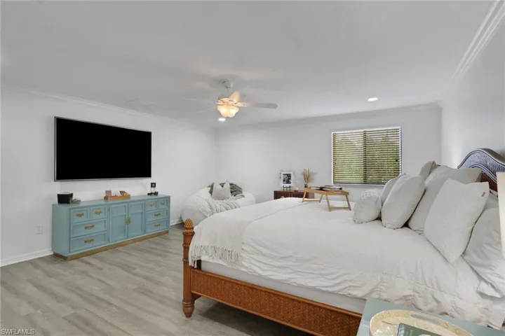 Neutral interior featuring wood-finish flooring, crown molding, a central ceiling fan with integrated light fixture, and horizontal window blinds