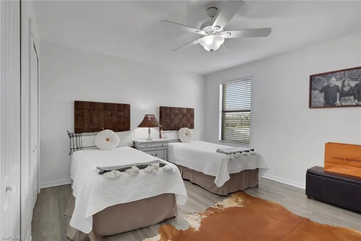 Neutral-toned interior space featuring wood-finish flooring, a ceiling-mounted light fixture with an integrated fan, and a single-panel window with horizontal blinds