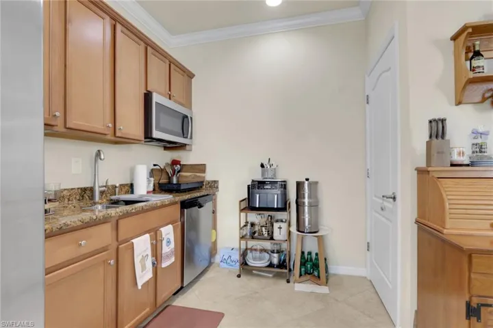 Light wood-finish cabinetry, stone countertops, stainless steel undermount microwave, stainless steel dishwasher, and arched-panel interior door