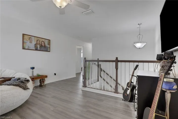 Wood-finish flooring, staircase with a wooden handrail and white balusters, ceiling fan with light kit, and polished metal pendant lighting