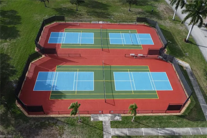 Dual recreational courts featuring multi-colored hard surfaces, perimeter chain-link fencing, and integrated net systems