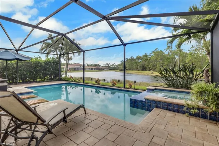 Screened lanai featuring a swimming pool, attached spa with tile finish, and paver patio overlooking a pond