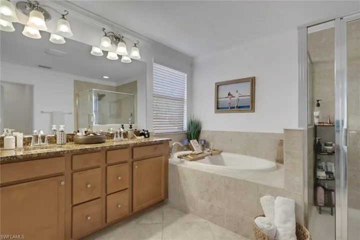 Bathroom featuring a dual-sink vanity with stone countertop, large wall-mounted mirror, soaking tub with tile surround, and an enclosed glass shower