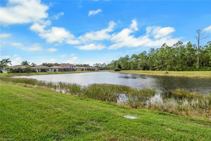 Waterfront property featuring a pond, manicured lawn, and native perimeter landscaping