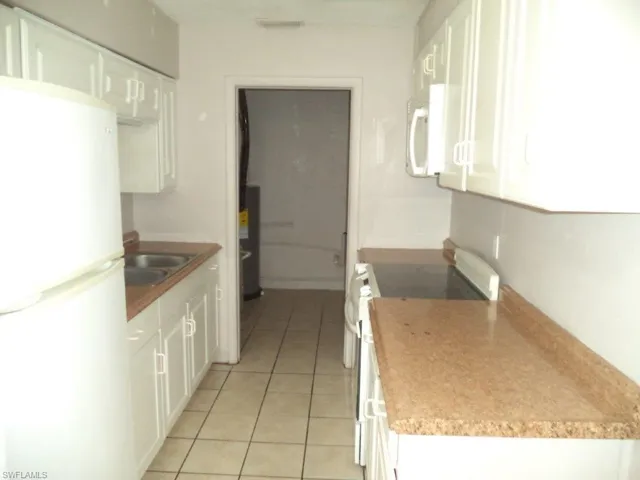 Kitchen featuring white appliances, white cabinetry, a sink, and light tile patterned floors