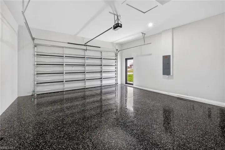 Spacious garage featuring a durable epoxy speckled flooring, an automatic garage door opener, a side entry door, recessed lighting, and a visible electrical panel