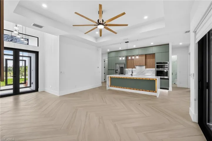 Open-concept living space featuring light wood-finish flooring in a herringbone pattern, a contemporary kitchen island with a quartz countertop, modern cabinetry, and recessed lighting