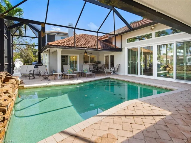 View of pool with glass enclosure, ceiling fan, and a patio area