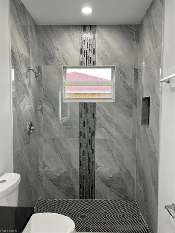 Shower stall with large format gray veined tile walls, linear mosaic accent strip, and a hinged window