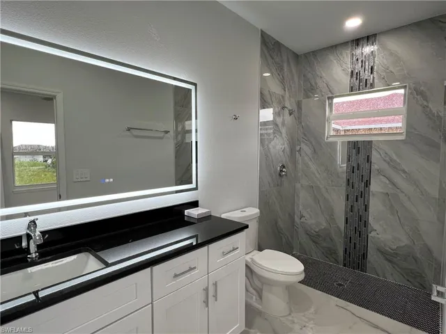 Bathroom featuring a lighted mirror, black countertop vanity with double-door cabinetry, and a walk-in shower with large-format tile and mosaic accents
