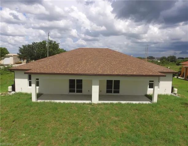 Rear exterior featuring a covered patio, multiple sliding glass doors, white stucco finish, and a brown shingle roof