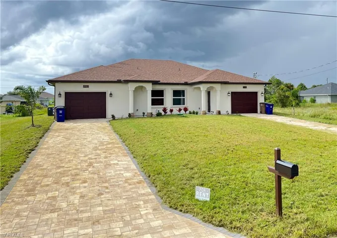 Duplex property featuring a neutral stucco exterior with contrasting brown garage doors and a coordinating shingle roof