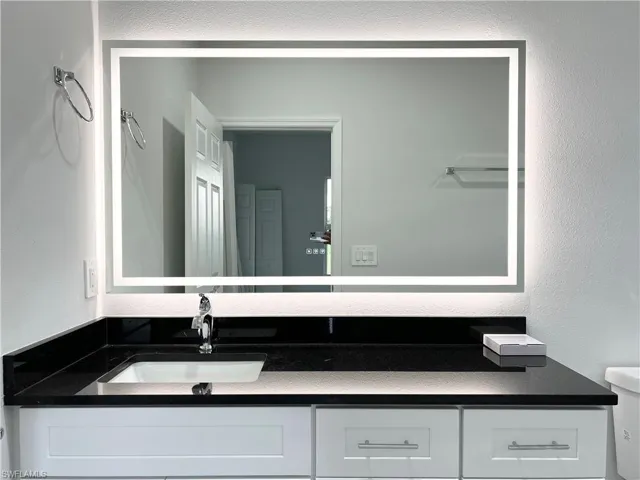 Vanity featuring a rectangular illuminated mirror, black countertop, undermount sink, and chrome faucet