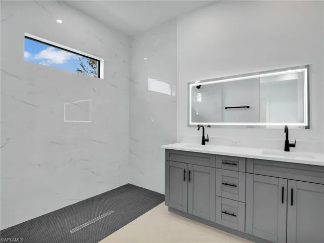 Bathroom featuring a tile shower, double vanity, and a sink