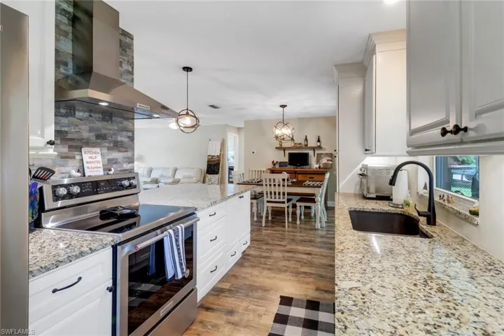 Kitchen with white cabinetry, range with two ovens, wall chimney range hood, and sink
