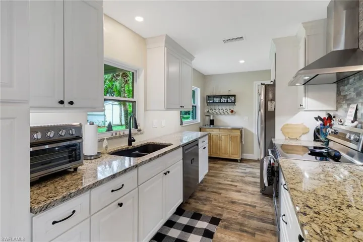 Kitchen featuring white cabinets, sink, wall chimney exhaust hood, dark hardwood / wood-style floors, and light stone counters