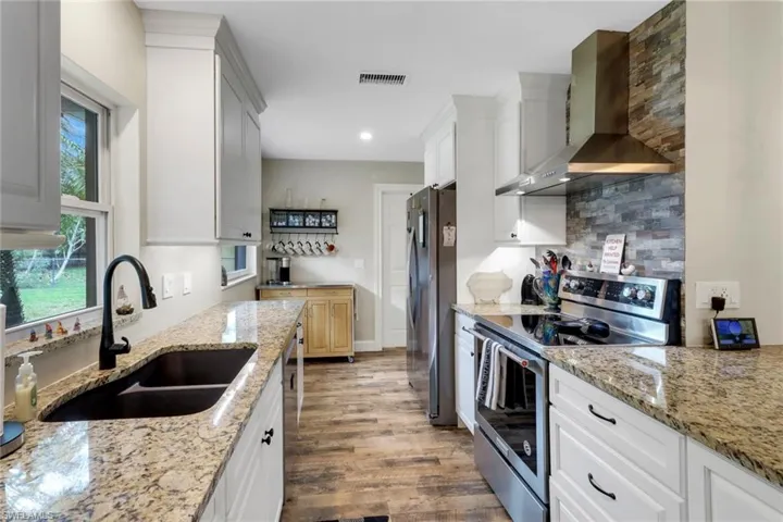 Kitchen with wall chimney exhaust hood, stainless steel appliances, sink, dark hardwood / wood-style floors, and white cabinetry