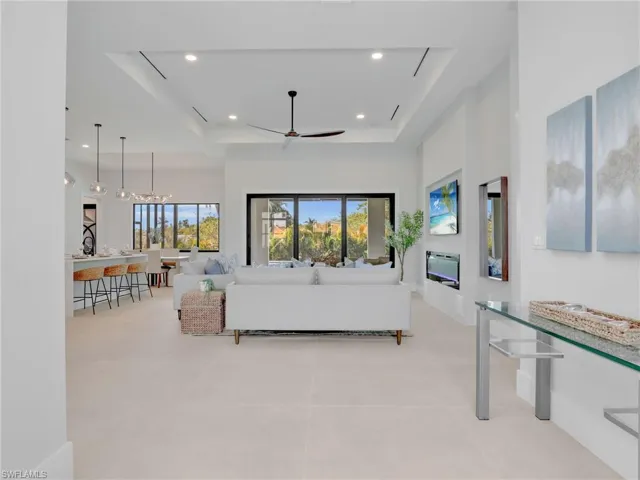 Living area featuring light tile patterned floors, ceiling fan, recessed lighting, a raised ceiling, and a glass covered fireplace