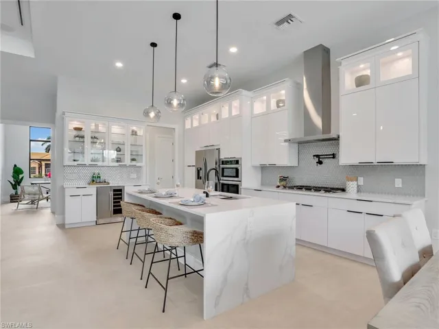 Kitchen with wine cooler, a breakfast bar area, visible vents, appliances with stainless steel finishes, and wall chimney range hood