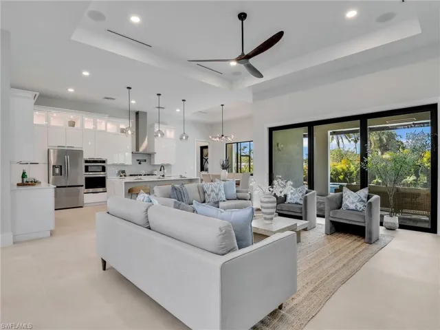 Living room with a tray ceiling, light tile patterned floors, recessed lighting, visible vents, and ceiling fan with notable chandelier