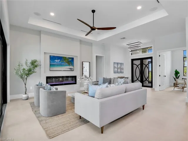 Living area with baseboards, a raised ceiling, a glass covered fireplace, a high ceiling, and recessed lighting