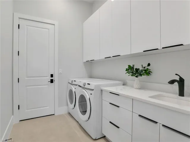 Clothes washing area featuring independent washer and dryer, cabinet space, a sink, and baseboards