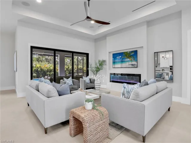 Living area featuring a tray ceiling, recessed lighting, a towering ceiling, a glass covered fireplace, and baseboards
