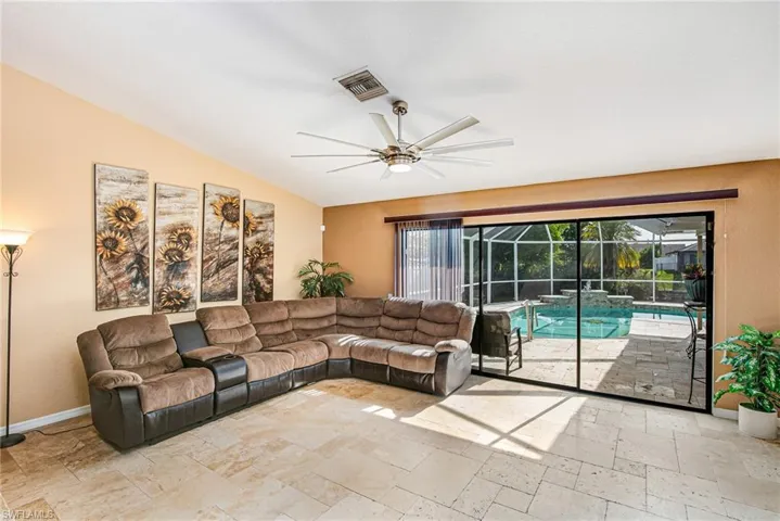 Living area featuring ceiling fan, vaulted ceiling, and stone tile flooring