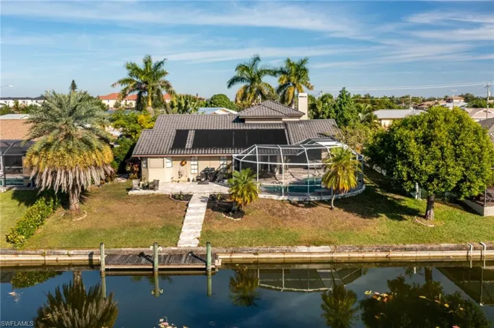 Rear view of property with glass enclosure, solar panels, a water view, a patio area, and a lawn