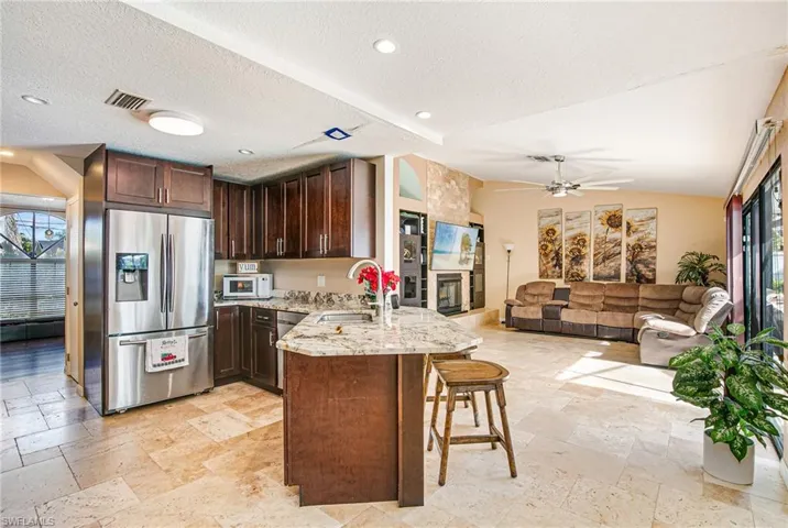 Kitchen featuring a peninsula, dark brown cabinetry, open floor plan, stainless steel refrigerator with ice dispenser, and light stone counters
