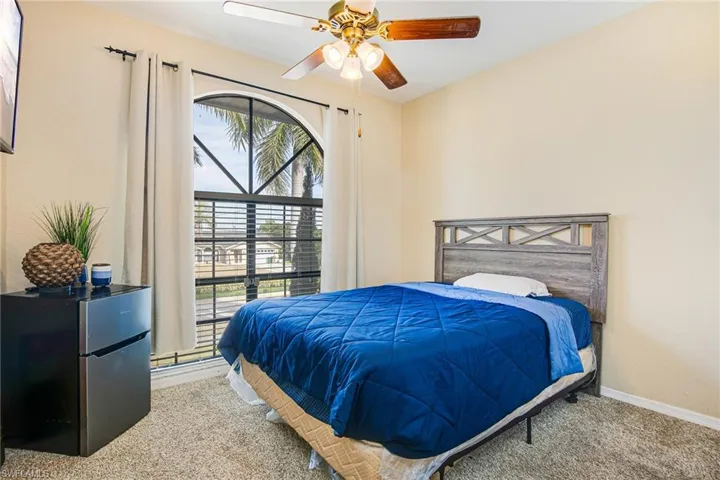 Carpeted bedroom with a ceiling fan and freestanding refrigerator