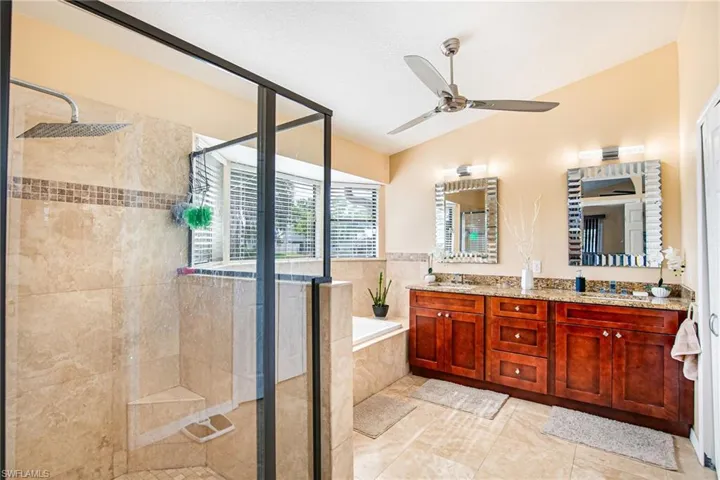 Full bathroom featuring a bath, double vanity, a shower stall, vaulted ceiling, and ceiling fan