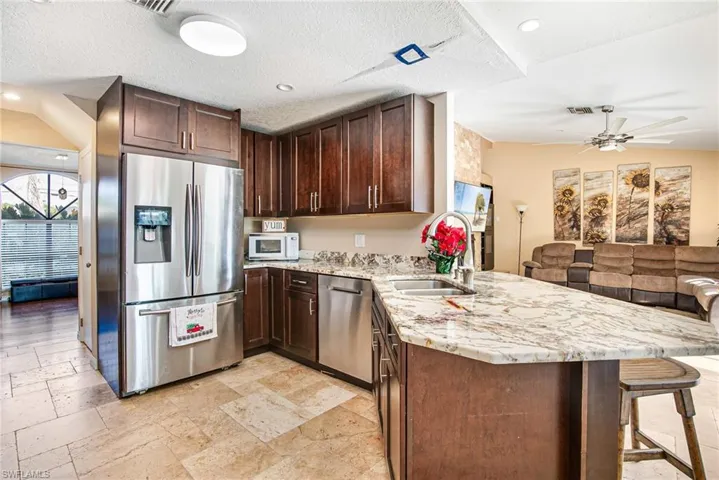 Kitchen featuring dark brown cabinetry, light stone counters, open floor plan, stainless steel appliances, and stone tile floors
