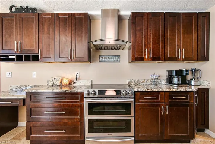 Kitchen featuring range with two ovens, wall chimney range hood, light stone countertops, a textured ceiling, and dark brown cabinets