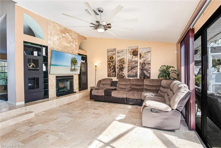Living area featuring stone tile flooring, ceiling fan, a fireplace, built in shelves, and vaulted ceiling