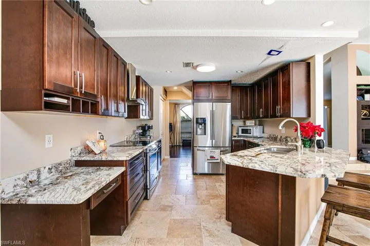 Kitchen with dark brown cabinetry, stainless steel appliances, light stone counters, recessed lighting, and a peninsula