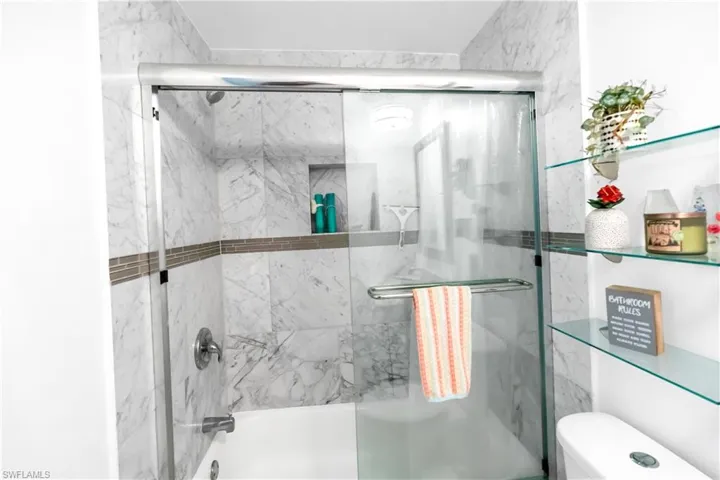 Bathtub and shower combination featuring marble-look wall tiles, a mosaic accent band, and a built-in shower niche