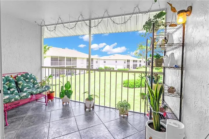 Screened patio featuring dark square tile flooring, white textured walls, and black metal railings overlooking a green lawn