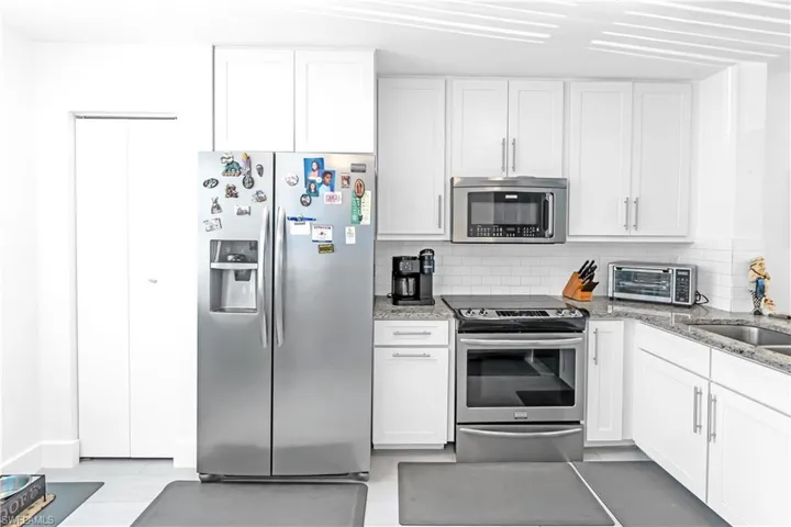 Modern kitchen featuring white shaker cabinetry, stainless steel appliances, speckled countertops, a subway tile backsplash, and light-toned flooring